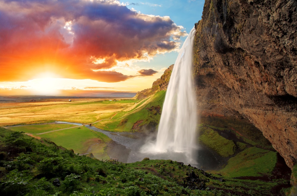 Seljalandsfoss, Iceland - flowing white waterwall in foreground, setting sun in background