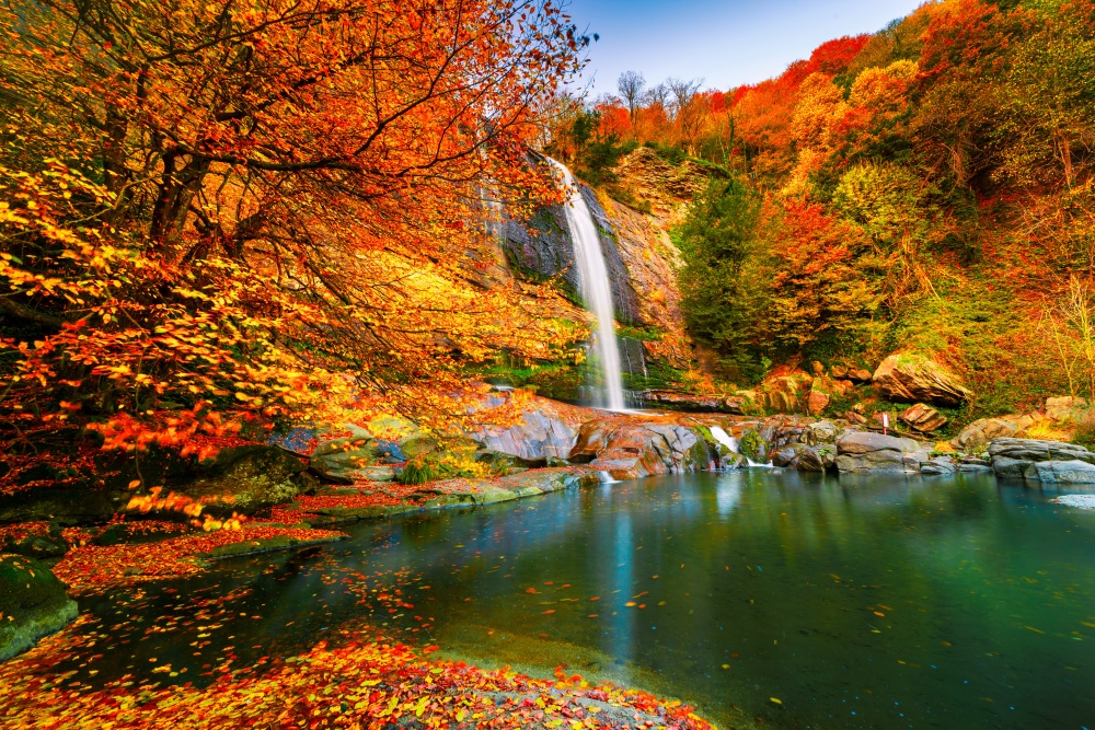 Waterfall surrounded by red and yellow autumn trees.