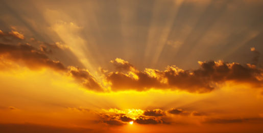 Rays of sunshine seen through clouds eminate from a warm orange sunset.